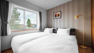 Una habitación de hotel con una cama grande, una mesita de noche, una lámpara y un ventanal con cortinas.