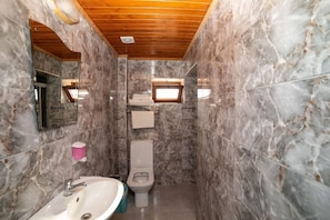 Et badeværelse med marmorvægge, træloft, håndvask, toilet og et vindue.