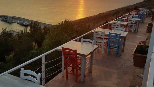 An outdoor terrace with tables and chairs, overlooking a body of water and distant mountains during sunset. - Gokceada Yakamoz Motel (Gökçeada)
