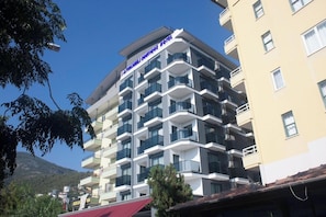 Un hotel de varios pisos con balcones, cielo despejado y una montaña al fondo.