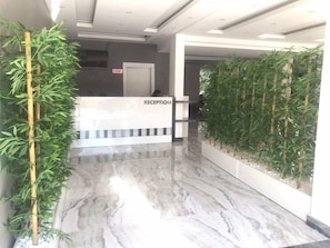 Un área de recepción con piso de mármol, mostrador de recepción y plantas de bambú.
