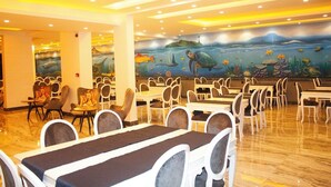 Restaurante com um mural de vida marinha na parede, várias mesas e cadeiras para refeições e piso lustroso.