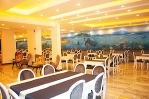 Un restaurante con un mural de vida marina en la pared, varias mesas y sillas para comer, y un piso pulido.