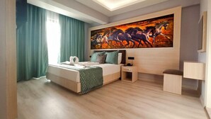 Quarto de hotel moderno com cama, mesa de cabeceira, escrivaninha e uma pintura grande na parede.