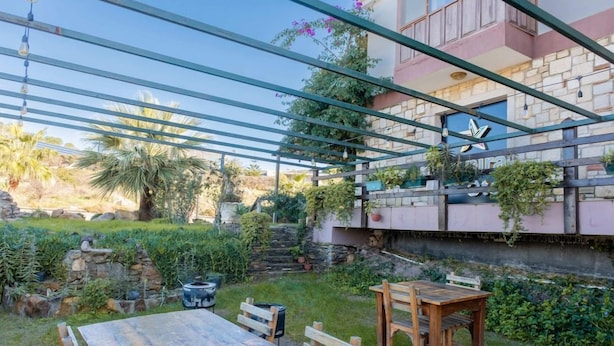 Una mesa de madera y bancos en un jardín con un muro de piedra y plantas.