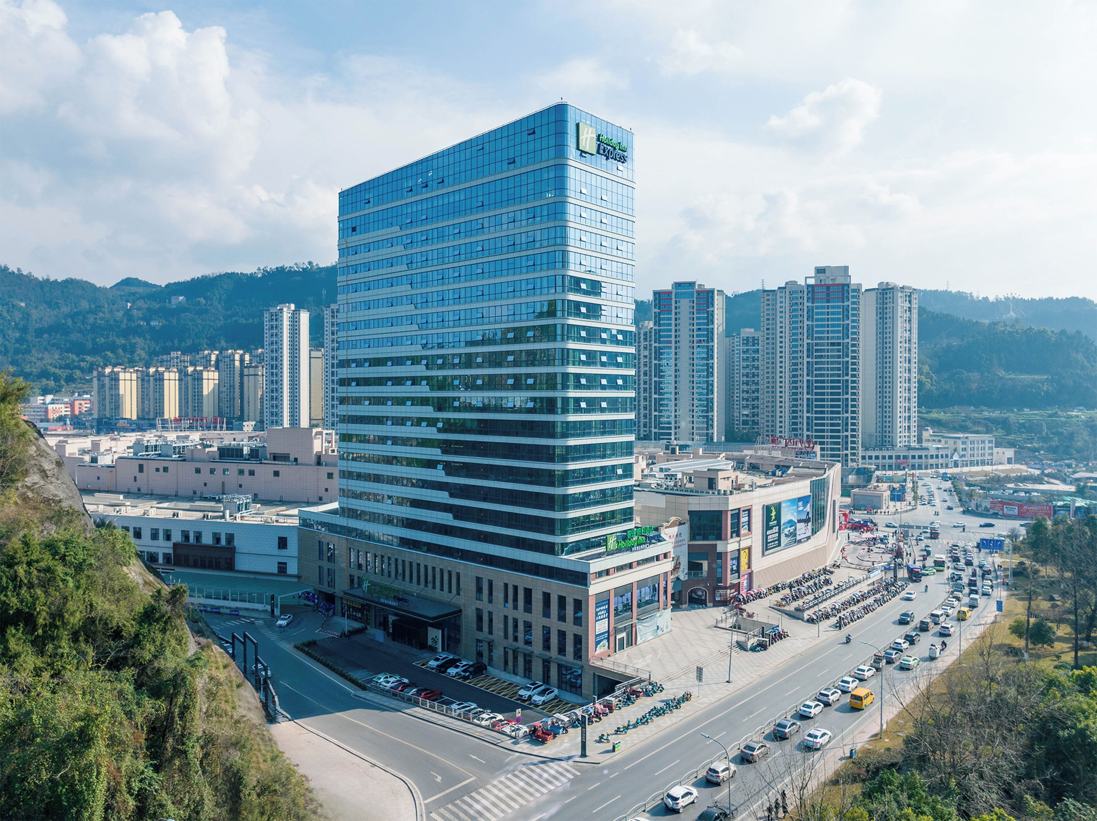 A modern hotel with a prominent glass facade, surrounded by a busy urban street and other high-rise buildings.
