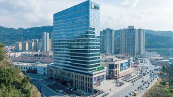 A modern hotel with a prominent glass facade, surrounded by a busy urban street and other high-rise buildings.