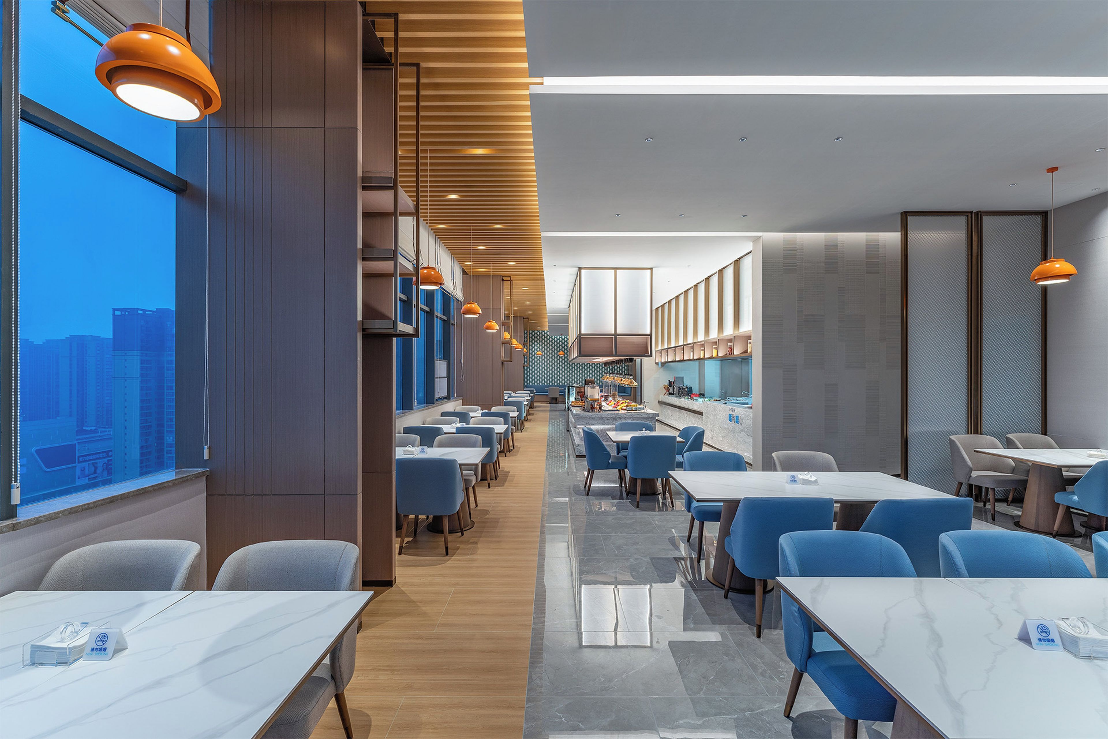 A modern restaurant with high ceilings, pendant lighting, and a view of the cityscape.