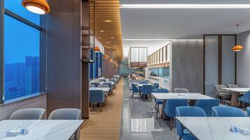A modern restaurant with high ceilings, pendant lighting, and a view of the cityscape.