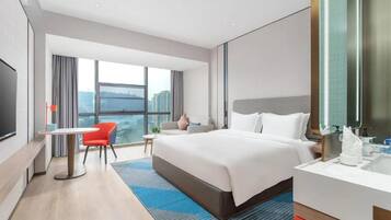A modern hotel room with a large bed, a desk, a chair, a TV, and a view of the city.