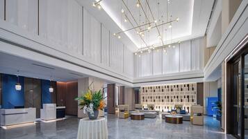 A spacious lobby with a high ceiling, modern lighting fixtures, and a seating area with sofas and round tables.
