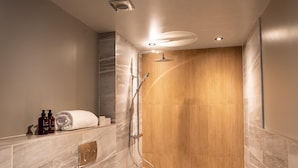 A modern bathroom with a shower, marble tiles, and a wooden panel wall. - Deira Hotel & Apartments (Prestwick)