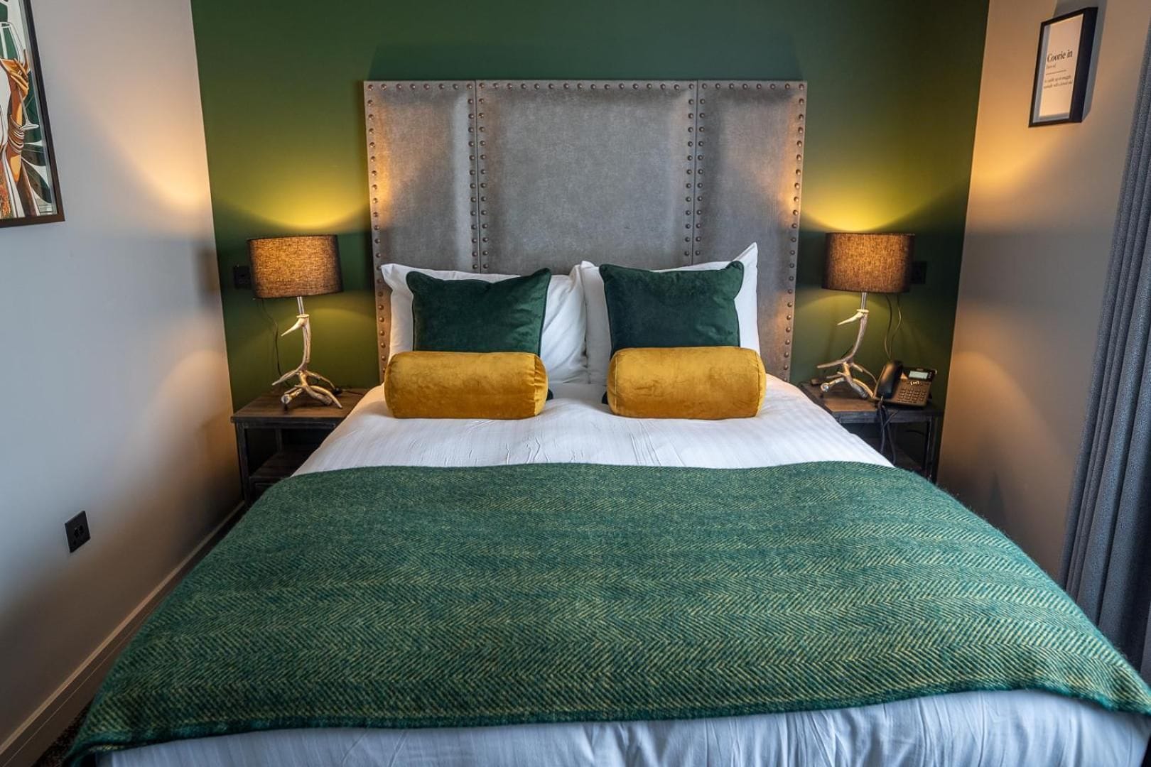 A hotel room with a large bed, two bedside lamps, and a green wall.