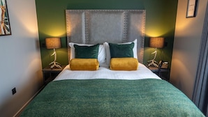 A hotel room with a large bed, two bedside lamps, and a green wall. - Deira Hotel & Apartments (Prestwick)