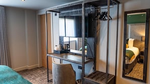 A hotel room with a bed, a desk with a chair, a mirror, and a television. - Deira Hotel & Apartments (Prestwick)