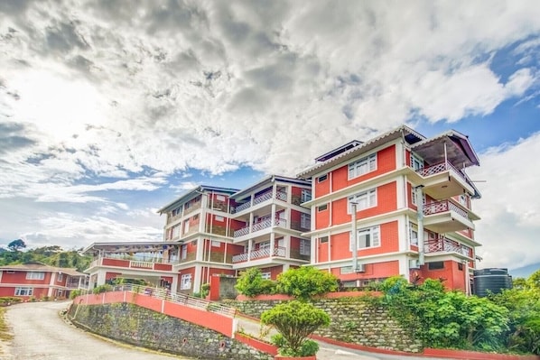 A multi-story building with balconies, a stone retaining wall, and a clear sky. - Summit Tashi Ghang Heritage Resort Pelling (Gyalshing)