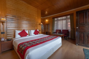 A hotel room with a large bed, a desk, and a chair. There is a wooden wall and a door visible. - Summit Tashi Ghang Heritage Resort Pelling (Gyalshing)