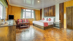 Quarto de hotel com cama, escrivaninha, televisão e janela com cortinas.