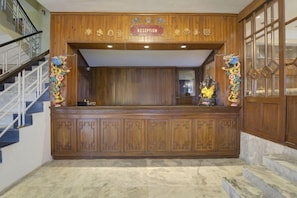 A reception area with a wooden reception desk, a staircase to the left, and a statue on the right. - Summit Tashi Ghang Heritage Resort Pelling (Gyalshing)