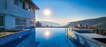 Una piscina infinita con vistas claras a las montañas, un edificio moderno con amplios ventanales y una superficie acuática tranquila.