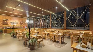 A restaurant with wooden tables and chairs, a brick wall with a counter, and large windows. - Hotel Crystal Pashupati (Kathmandu)