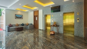A modern lobby with a marble floor, a sofa with cushions, a small table with a decorative item, and two elevators. - Hotel Crystal Pashupati (Kathmandu)
