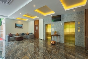 En moderne lobby med et marmorgulv, en sofa med puder, et lille bord med en pynteting, og to elevatorer.