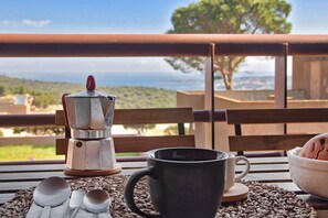 Un tavolo con una macchina per caffè, una tazza nera e una ciotola di pane su un balcone con vista panoramica.