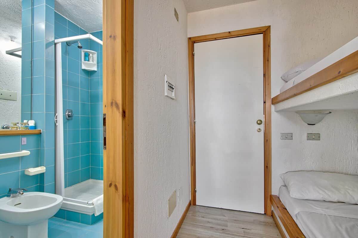 Casa de banho com chuveiro, pia e porta que dá para um quarto com beliche.