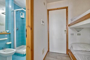 Un bagno con doccia, lavandino e una porta che dà su una camera con un letto a castello.