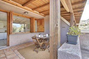 A covered outdoor dining area with a wooden table and chairs, a potted plant, and a view of the surrounding landscape. - Studio Apartment in the Heart of the Costa Smeralda (Olbia)