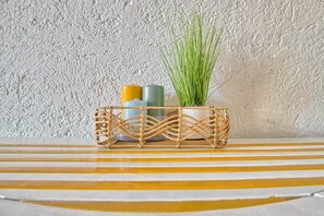 A woven basket with a potted plant and two candles on a striped surface against a textured wall. - Studio Apartment in the Heart of the Costa Smeralda (Olbia)
