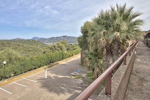 A paved road with a guardrail, a palm tree, and a view of a hilly landscape. - Studio Apartment in the Heart of the Costa Smeralda (Olbia)