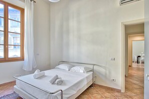 Un llit individual amb estructura metàl·lica, roba de llit blanca i una tovallola enrotllada al capçal.