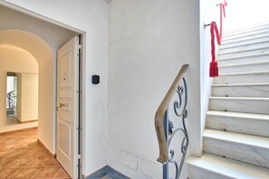 Un passadís amb una porta blanca, una escala amb trams de marbre i un gronella vermell a la barana.