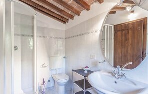 Casa de banho com chuveiro, sanita, lavatório e porta de madeira.