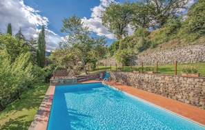 Ein Pool mit einer Steinmauer und einer Rasenfläche mit Bäumen.