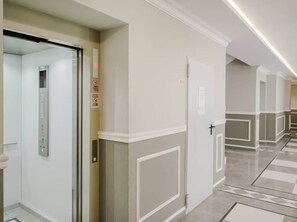 Un couloir avec une porte, un ascenseur fixé au mur et un sol carrelé.