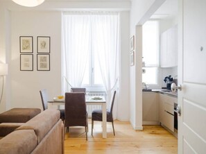 A modern living room with a dining area, a kitchen, and a view through a window with sheer curtains. - In the Heart of Florence, Just a Stone's Throw from the Duomo (Florence)