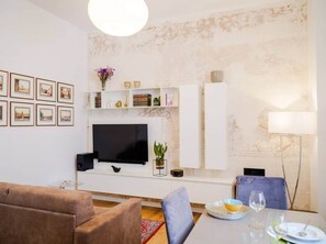 Un salon moderne avec un téléviseur à écran plat, des meubles blancs, une table à manger avec des chaises et un canapé.