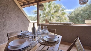 Een eettafel met borden, glazen en bestek, onder een houten pergola met uitzicht op palmbomen.