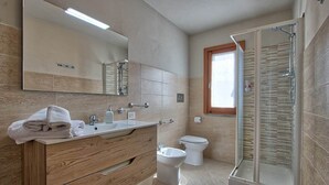 Et moderne badeværelse med et trækommode, et glasbadeværelsesafskærmning, et toilet og et stort spejl.
