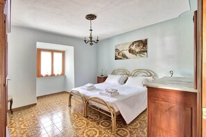 Ein Schlafzimmer mit einem Bett, einem Nachttisch, einer Chandelieber, einem Fenster und einem Gemälde an der Wand.