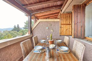 An outdoor dining area with a wooden table set for four, surrounded by woven chairs, with a view of trees and hills in the background. - Comfort and relaxation in the heart of the Costa Smeralda (Cugnana Verde)