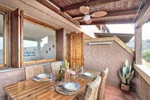 A dining area with a wooden table set for four, surrounded by wicker chairs, a ceiling fan, and a view of the landscape. - Comfort and relaxation in the heart of the Costa Smeralda (Cugnana Verde)