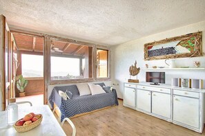 A cozy room with a bed, a dining table with fruit, a TV, and a rustic wall art piece. - Comfort and relaxation in the heart of the Costa Smeralda (Cugnana Verde)
