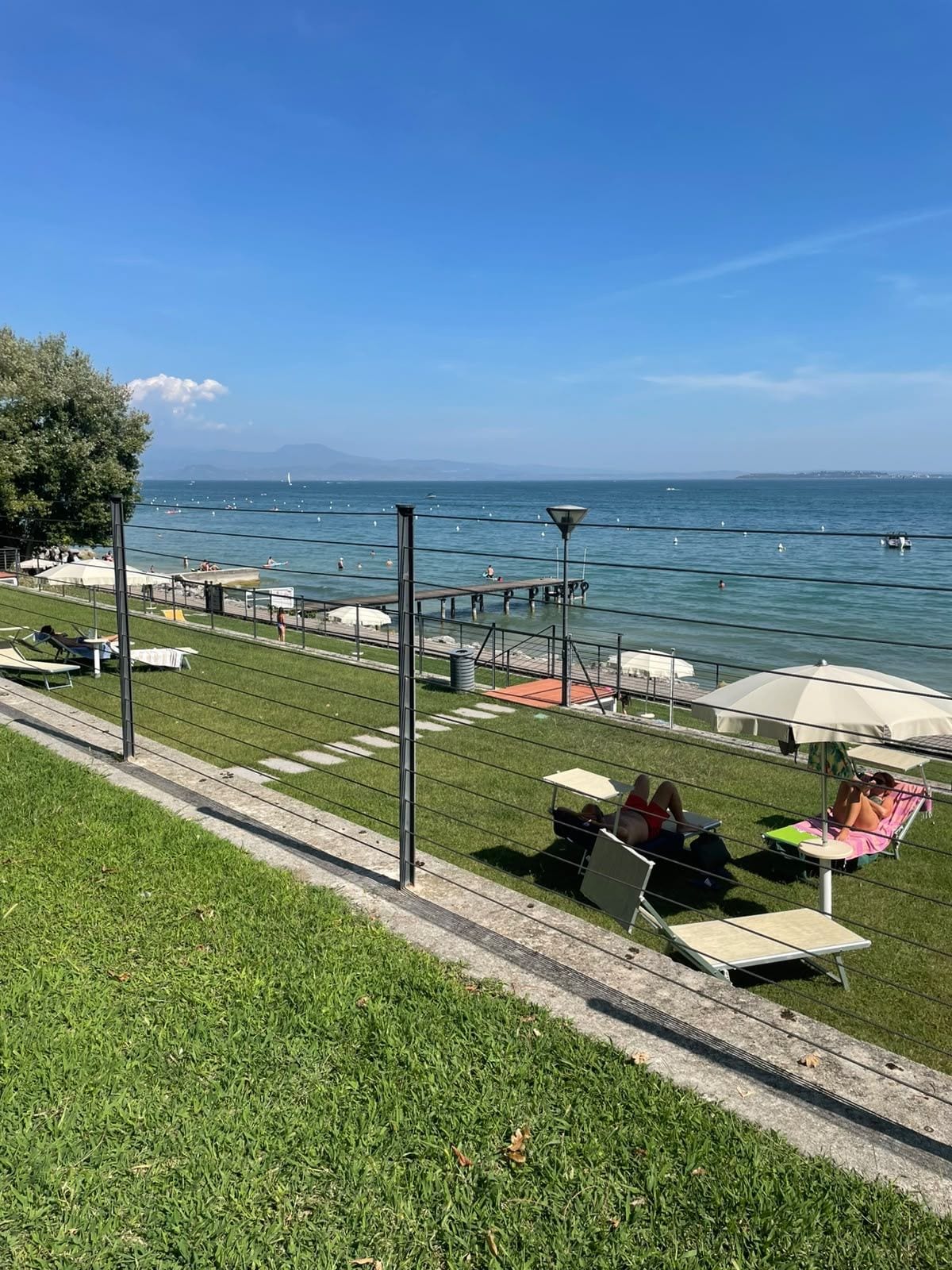 A waterfront promenade with grass, seating areas, and a view of the sea.