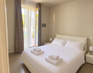 A hotel room with a large bed, two bedside tables, a window with curtains, and a view of greenery outside. - Gardazzurro—Vacation Rental on Lake Garda with a Pool & Tennis Court (Padenghe Sul Garda)