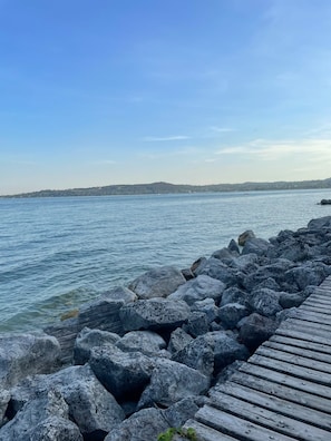 A wooden pier extending into calm water, surrounded by large rocks. - Gardazzurro—Vacation Rental on Lake Garda with a Pool & Tennis Court (Padenghe Sul Garda)