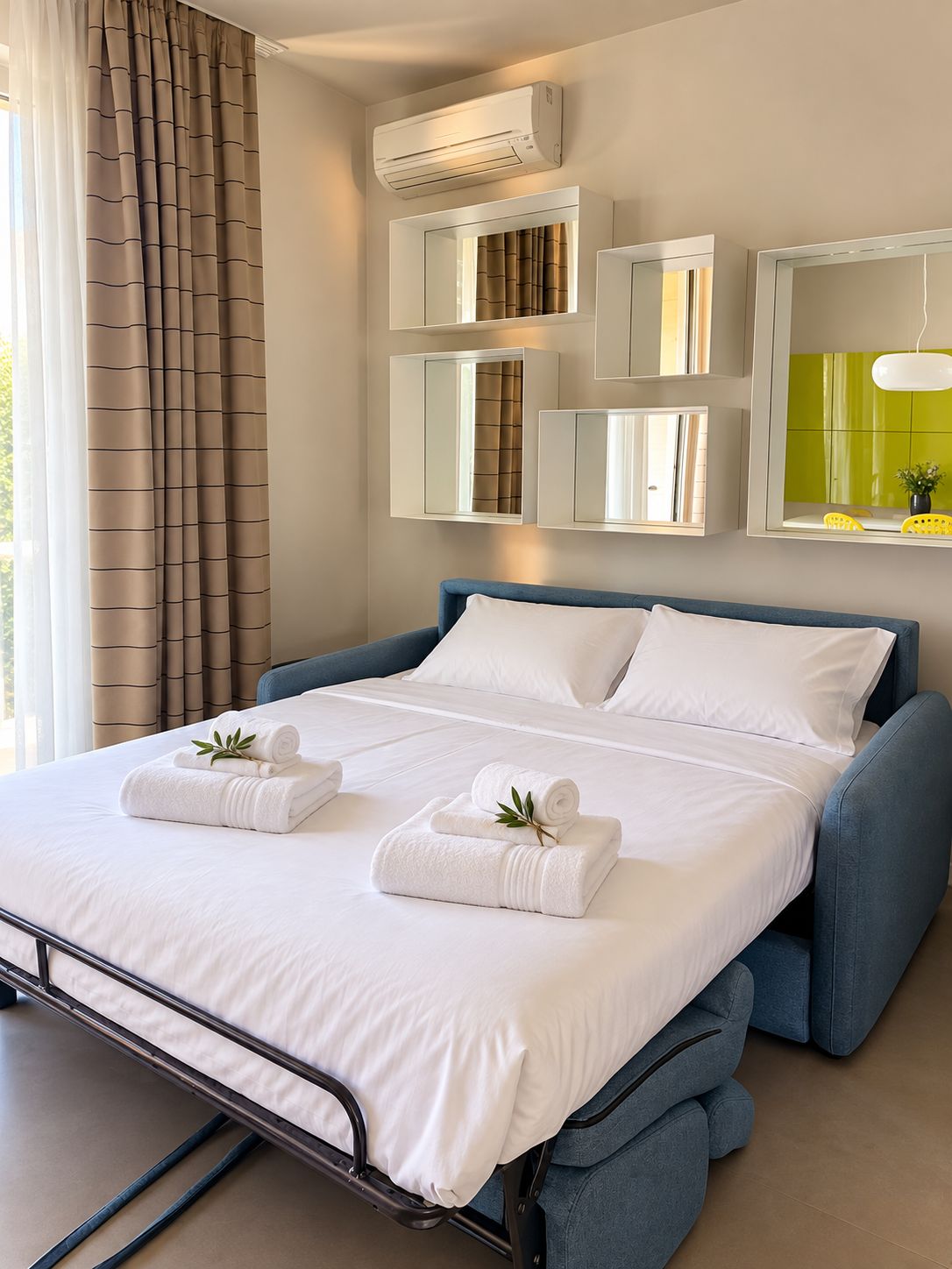 A hotel room with a bed, white linens, a blue headboard, and a wall-mounted air conditioner.